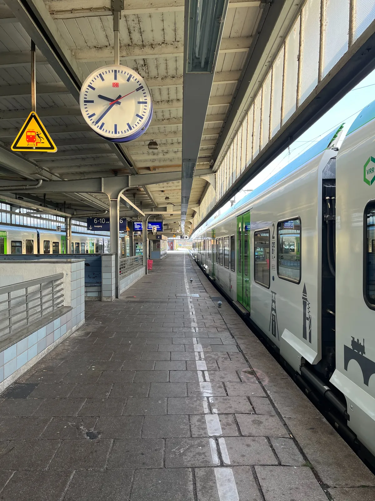 A train is parked on the platform. The clock that hangs from the ceiling points at 37 minutes past 9.
