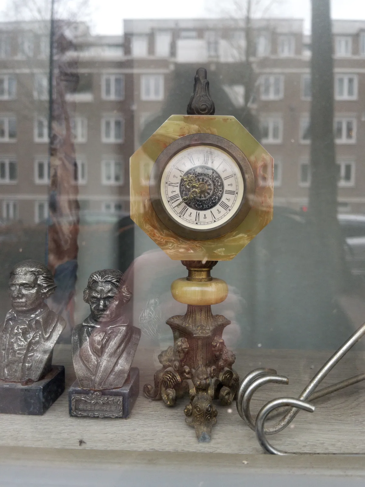 Two little busts of stern looking men behind a window. There’s also a clock made from metal and stone. It points at 38 minutes past 9.