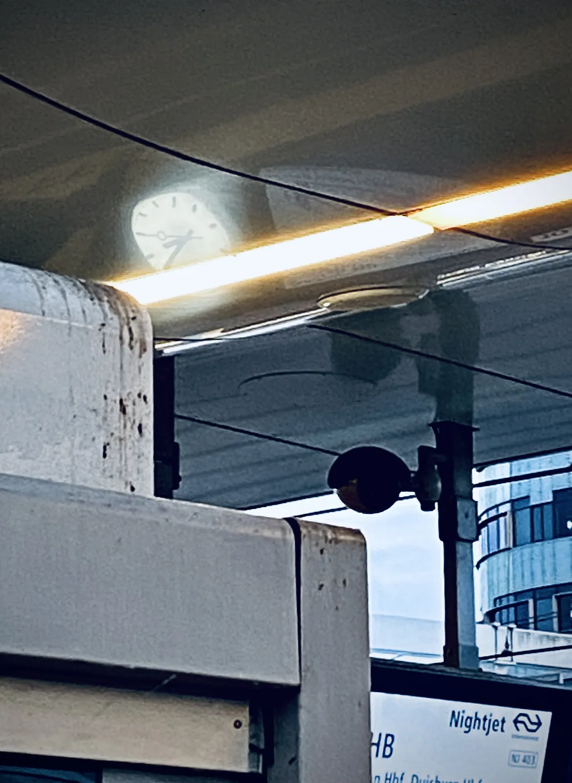 A clock is mirrored in this weird shiny ceiling. It seems to point at approximately 20 to ten. 