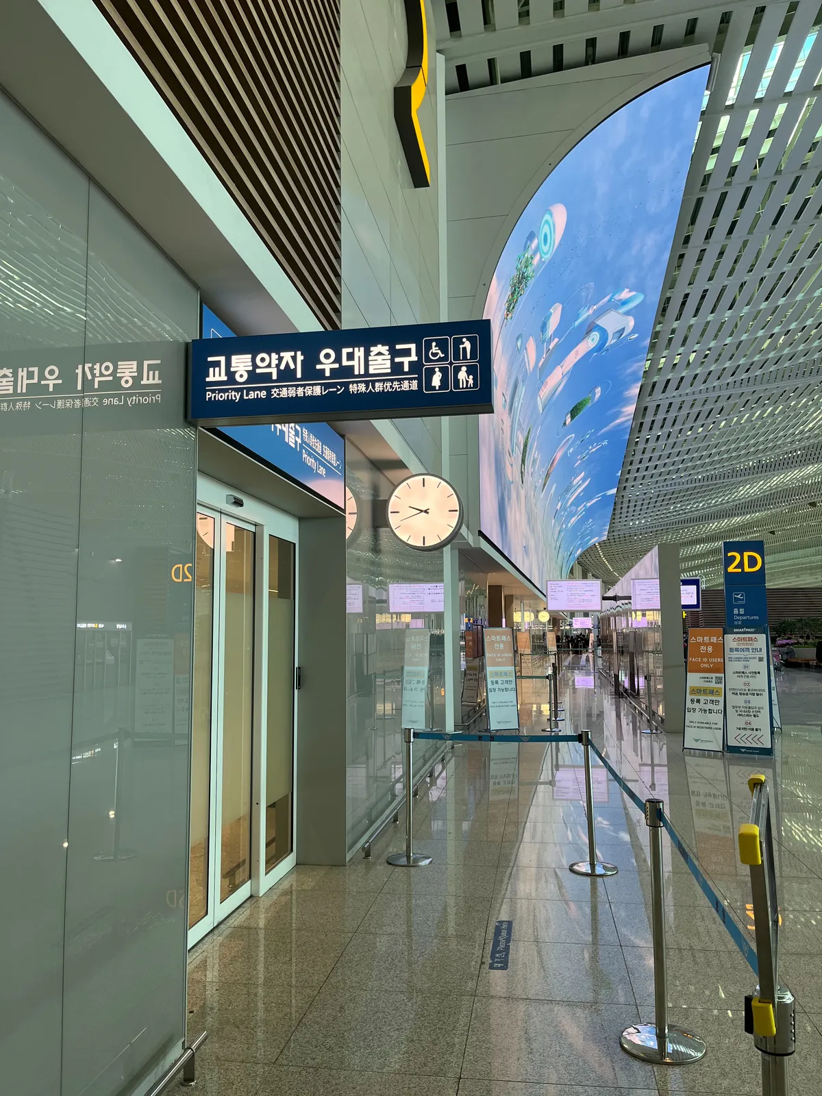 Nobody is waiting at this priority line sign in this Korean airport. A gigantic curved screen hangs on the wall in the enormous terminal. And there is a clock, which points at 18 minutes to 10.