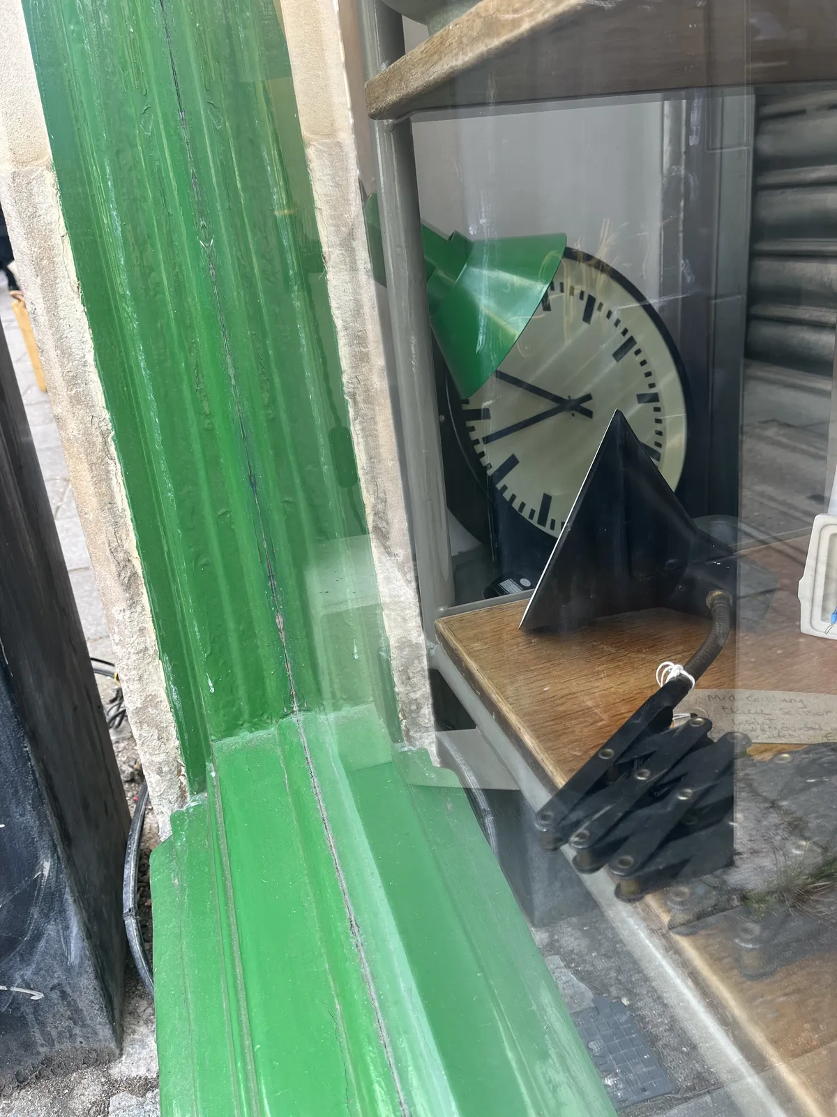 A modernist station clock leaning against the wall in a second had lamp shop. Since the indicators on the clock don’t show where the twelve is, it could be almost any time. But by assuming the twelve is up, it is now 17 minutes to ten. 