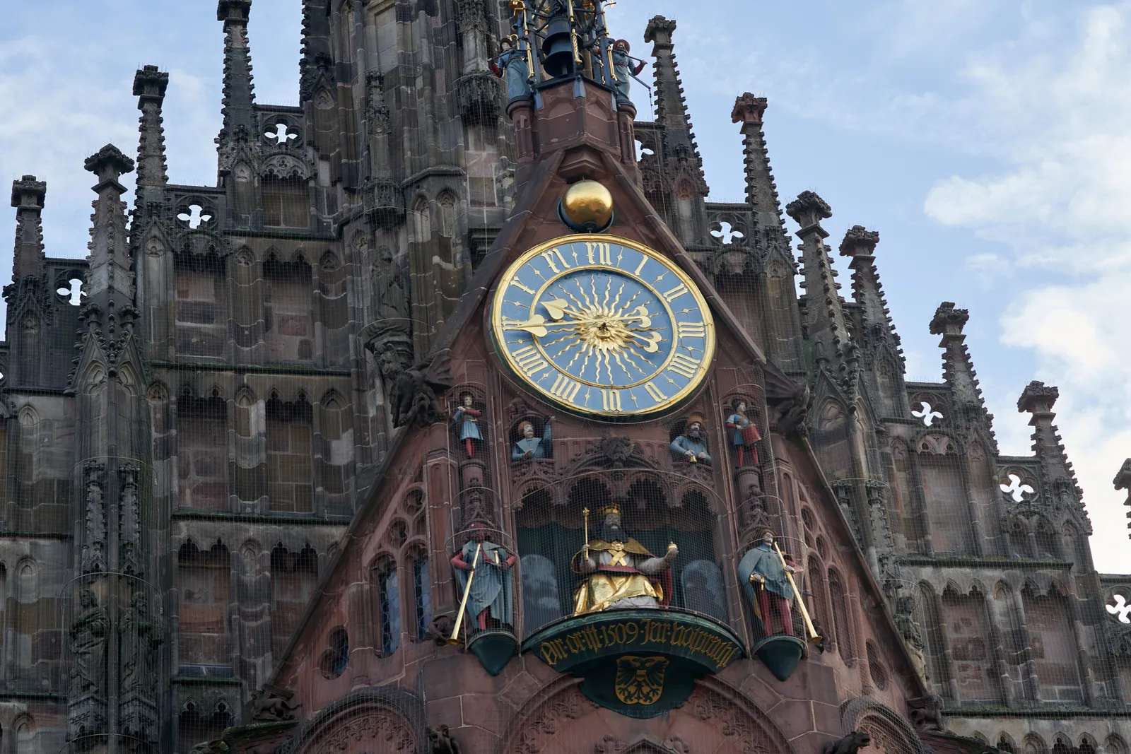 A very busy church with a very colourful and shiny clock on it. It points at 16 minutes to 10.