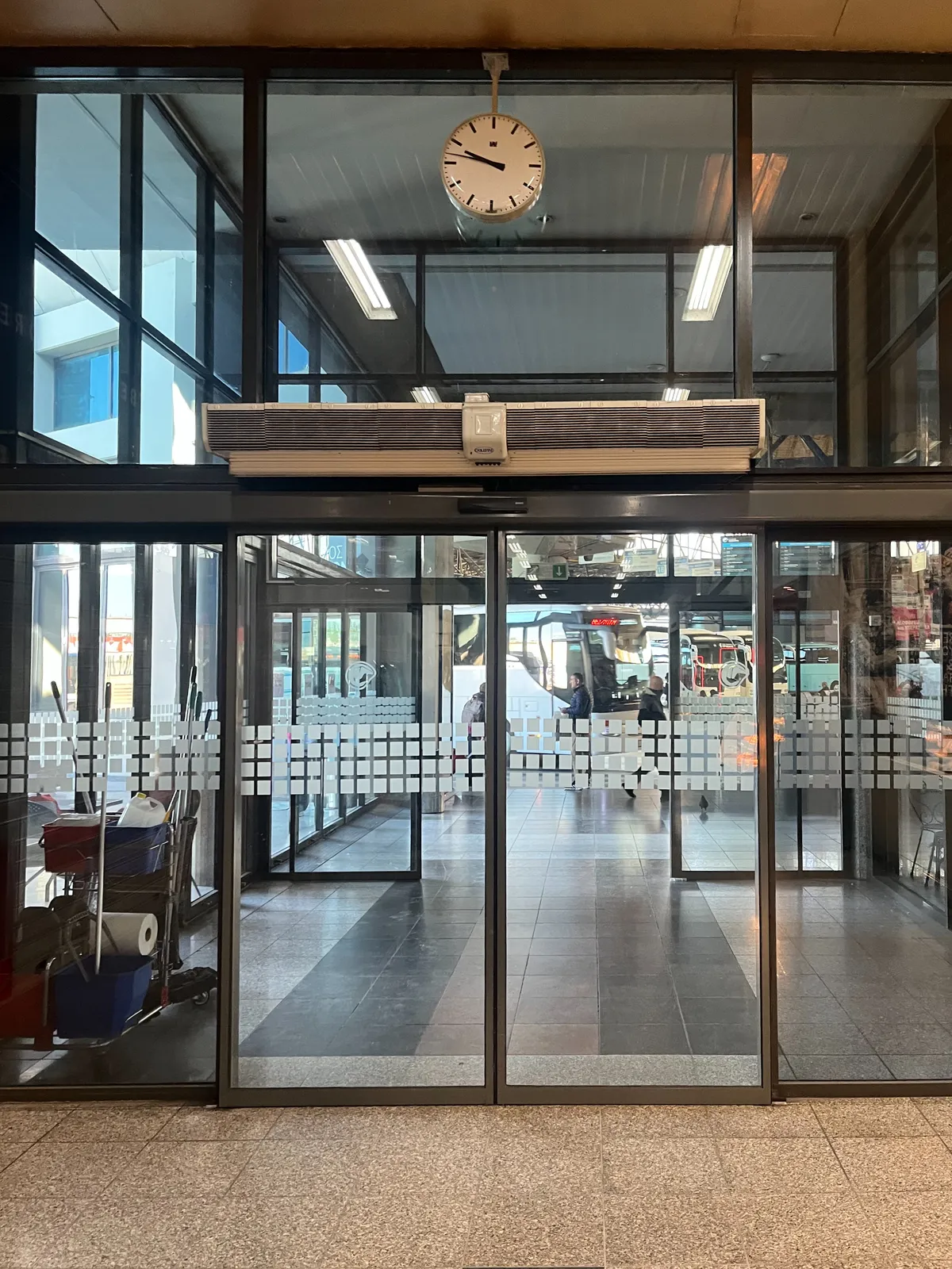A clock above a glass door. It points at 13 minutes to ten.