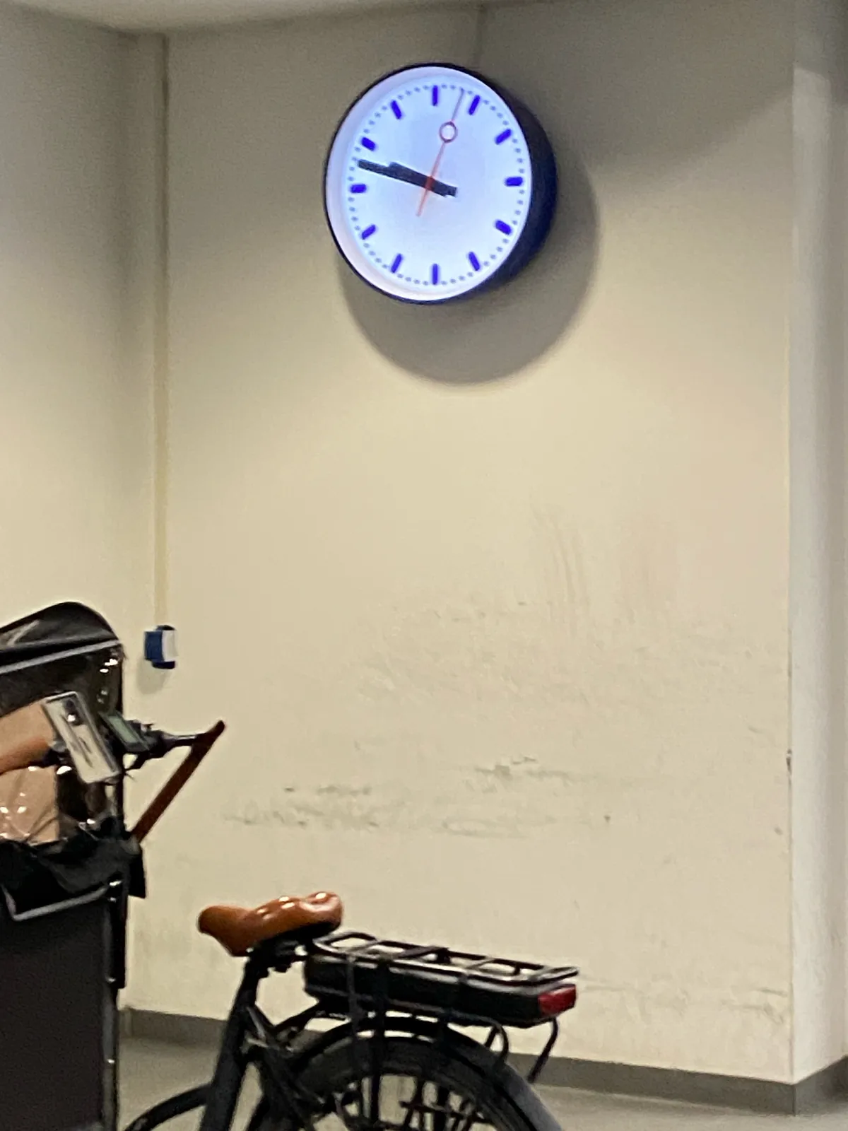 Part of a cargo bike can be seen. And there’s a clock on the wall which points at 13 minutes to 10.