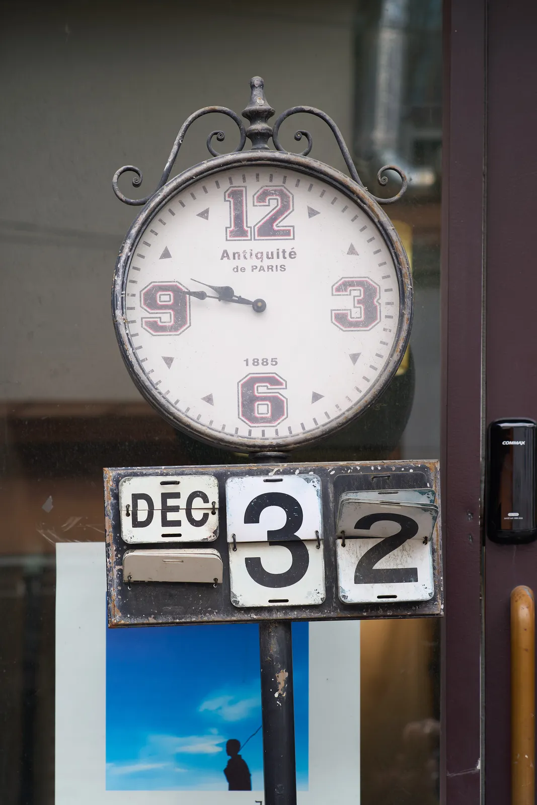 A strange clock. It says antiquité de Paris, 1885 on its face. The numbers 3, 6, 9 and 12 are printed in, what I think are called american college fonts. Below the clock there’s a rusty flip calendar which says it is December 32. Which is not true. The clock itself points at 13 minutes to 10.