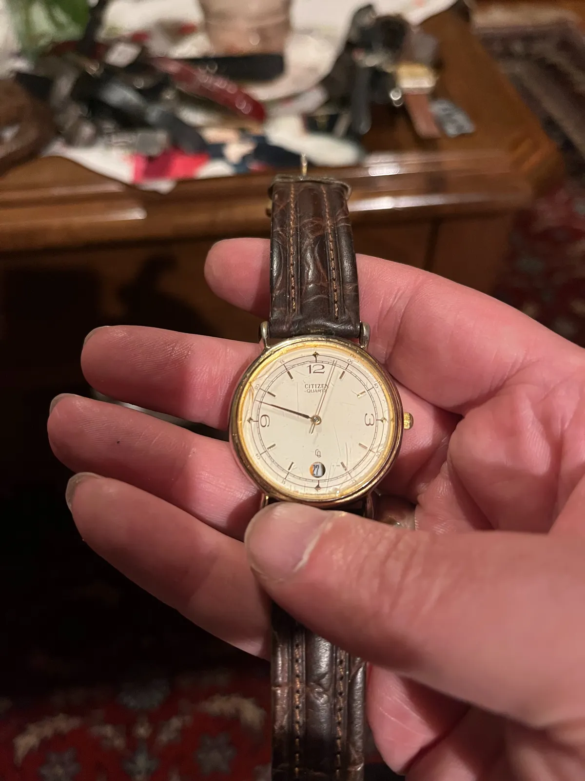 Someone is holding an old watch in their hand. In the background, blurry, an old Persian rug. The watch points at twelve minutes to ten.