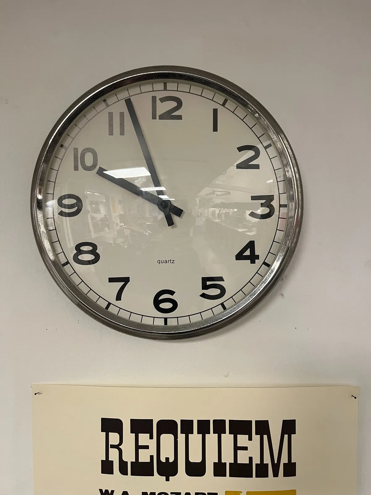 The word “requiem” is printed with a western typeface on a poster. Above this poster there’s a clock that points at 9 minutes to 10.