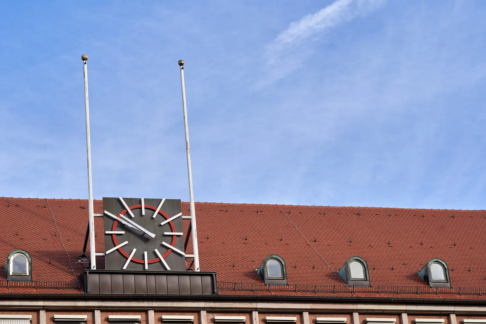 A quite modern, large, black and white clock on the roof of a building. It pointa at 9 minutes to 10.