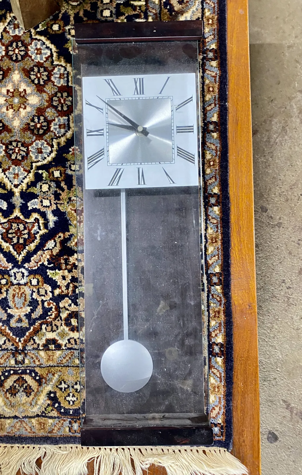 A modernist clock with a pendulum which is weirdly aligned to the left, instead of the center where you would expect it. The clock points at 8 minutes to 10.