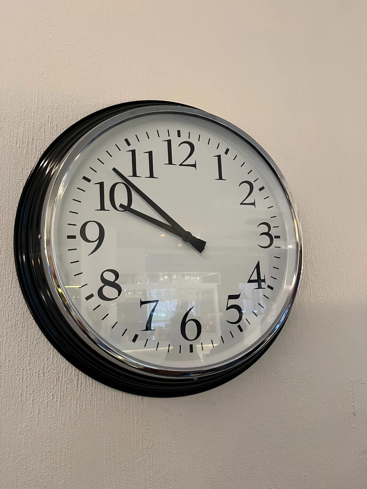 A modern clock on a white wall. It points at 8 minutes to 10.