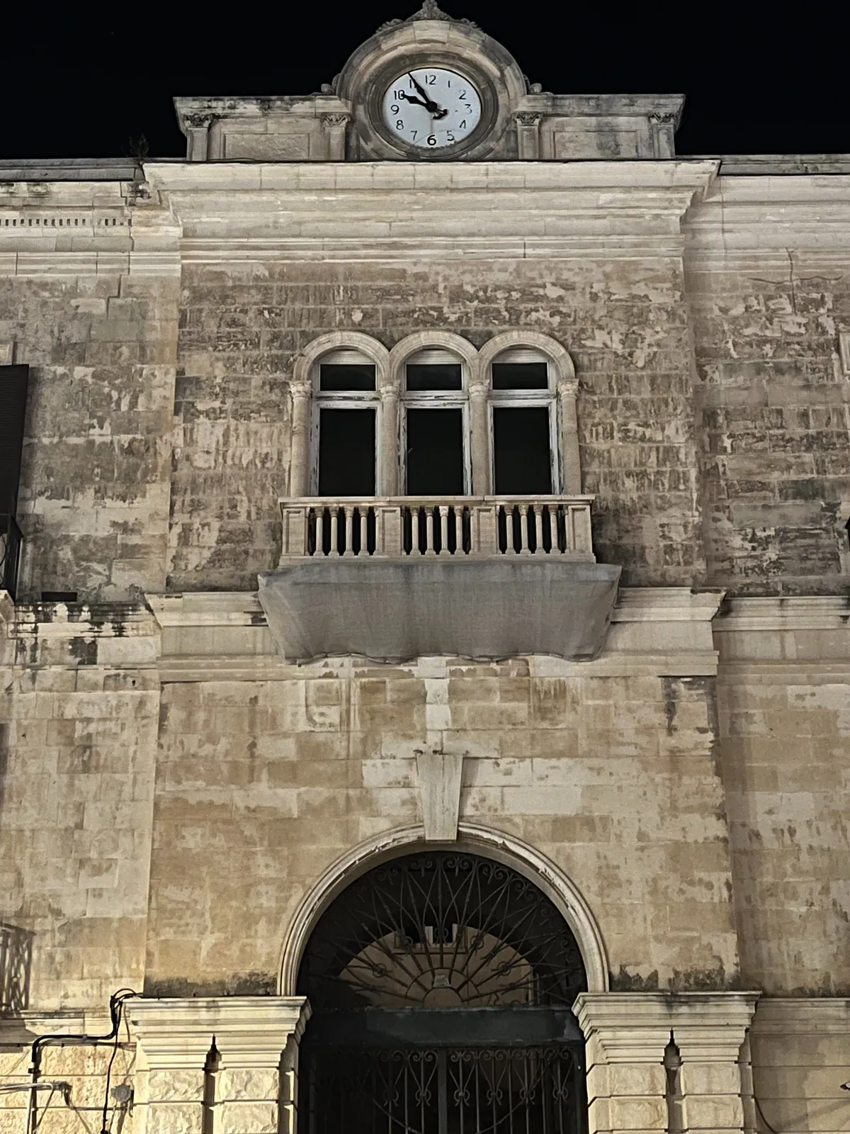 An old, white, stone building with a clock. The clock points at 5 to 10.