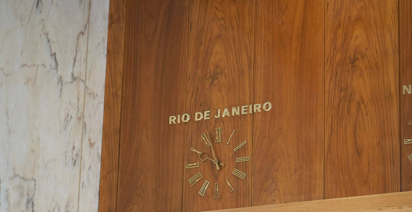 A lathed wall with a built in clock. Above the clock it says Rio de Janeiro. The clock points at 3 minutes to 10.