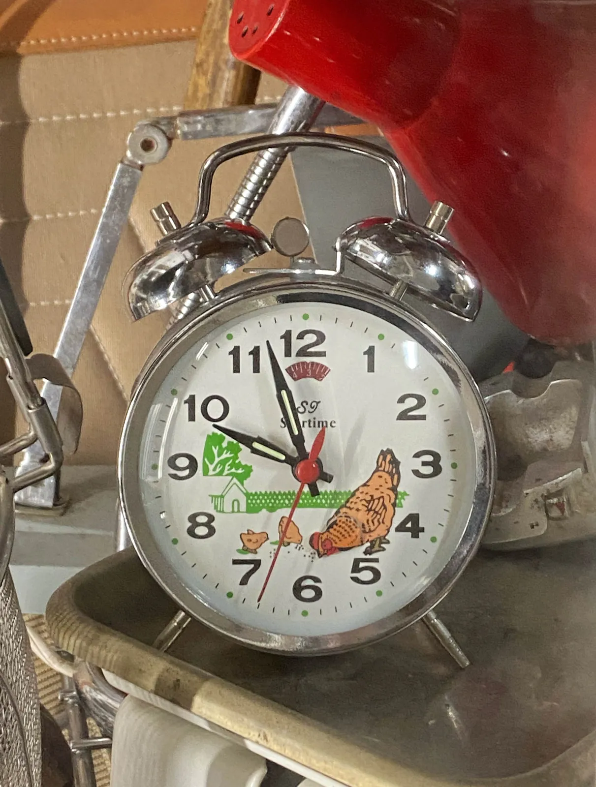 An old mechanical alarm clock with an image of a hen and to chicks on it. It points at 3 minutes to 10.