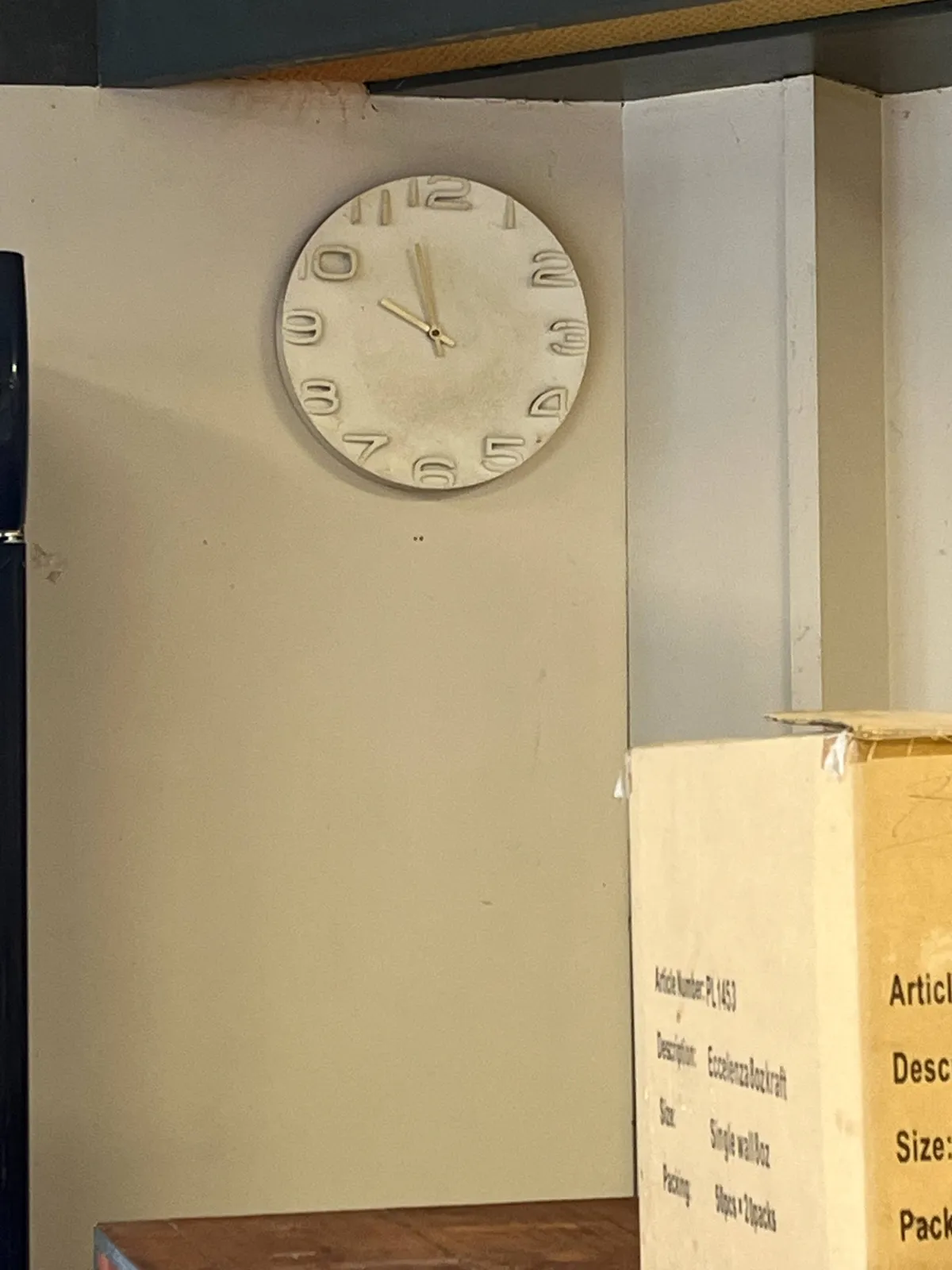 A white clock on a white wall. It points at 3 minutes to 10.