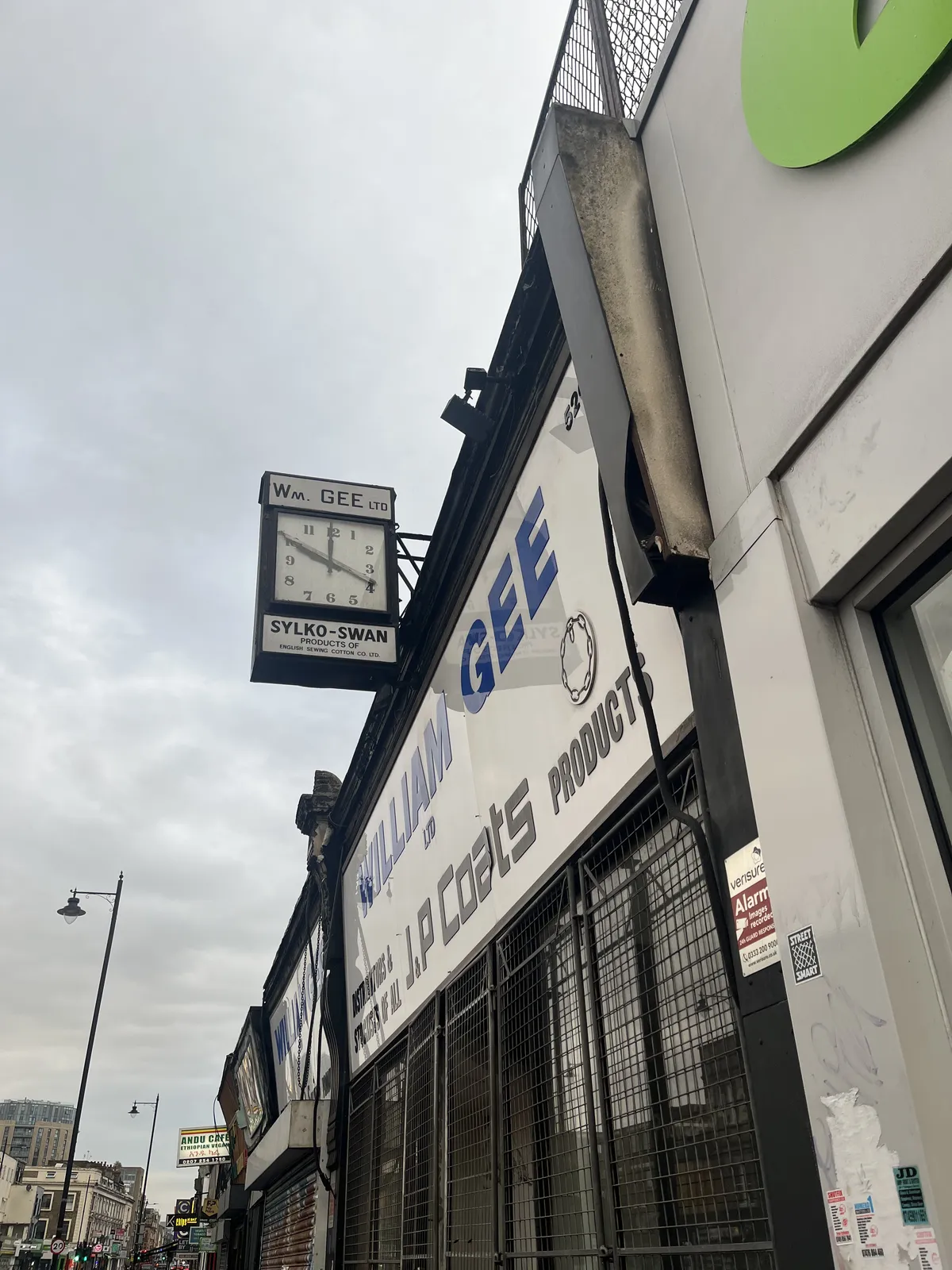 A clock attached to the shop of William Gee, as it says on the huge plastic facade, and on the clock itself. The clock points at one minute to ten.