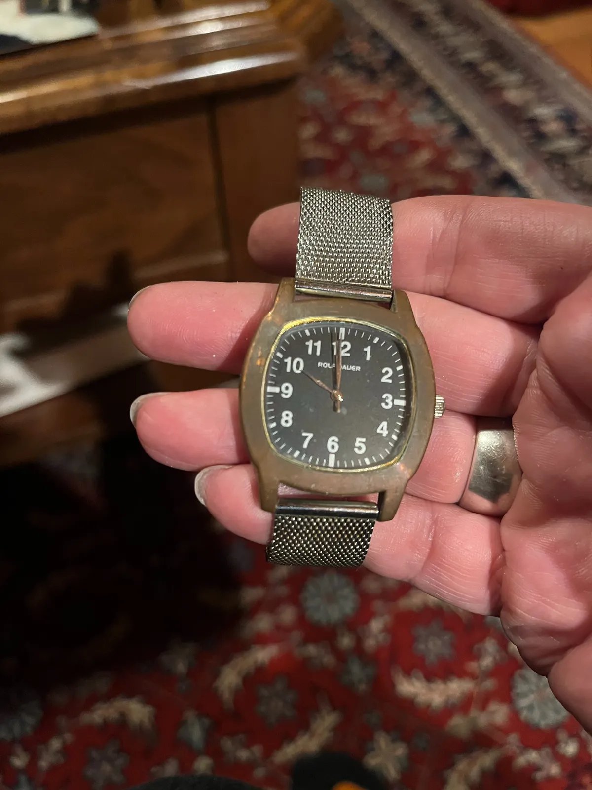 Someone is holding an old watch in their hand. In the background, blurry, an old Persian rug. The watch points at ten o’clock.