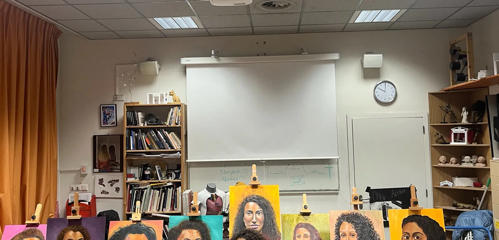 An art classroom. The upper parts of some paintings can be seen, and a clock on a wall which points at one minute past 10. 