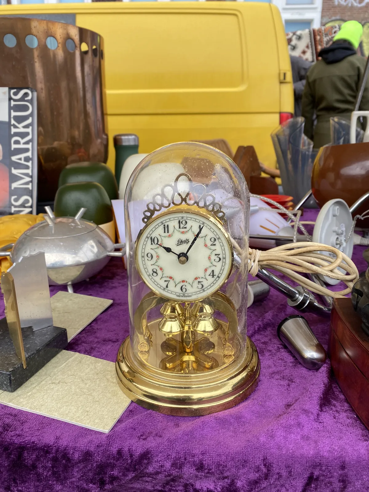 All kinds of stuff for sale on this flea market. One of the things is a gold plastic clock in a glass plastic dome which points at 5 past 10.