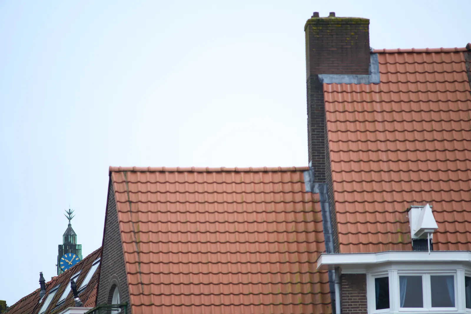 A rather weird church tower peeks over the roofs of a few buildings in Amsterdam. The clock on the weird tower points at 5 past 10.