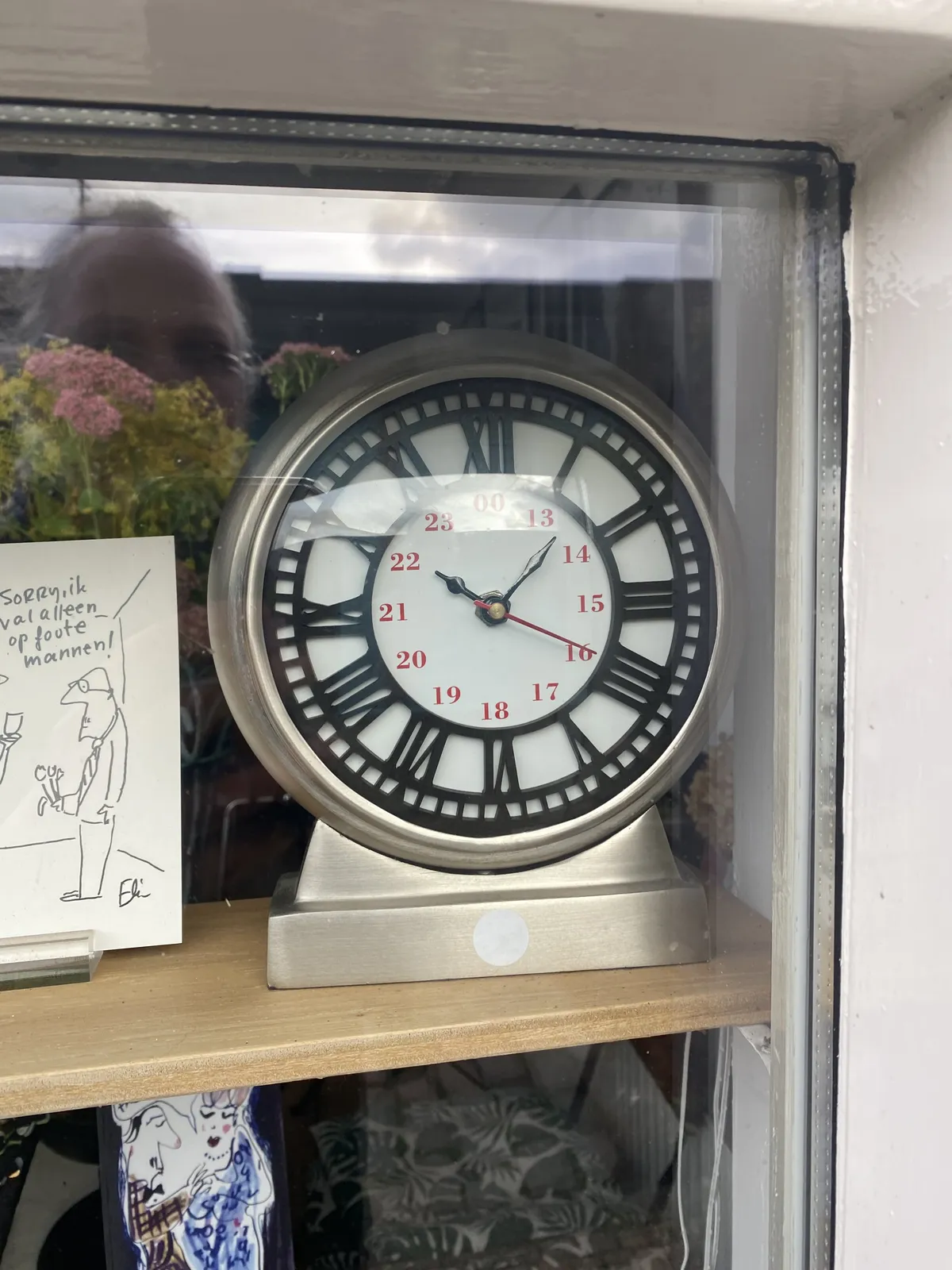 A standing clock behind a window. In the reflection the photographer can be seen. The clock is black and white. It points at 7 minutes past 10.
