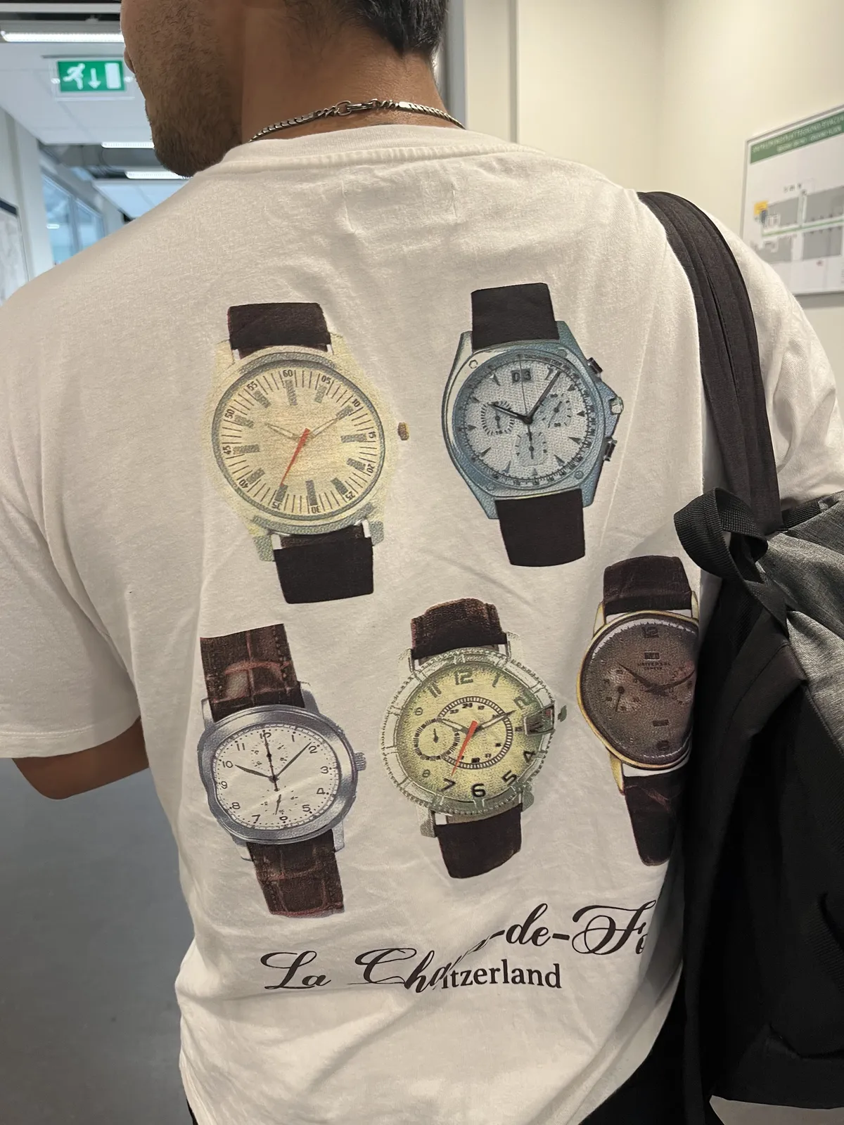 Someone is wearing a white t-shirt with on the back five wrist watches. Three of them point at ten past ten, one of the points at 6 minutes past ten, and the other points at 8 minutes past ten.