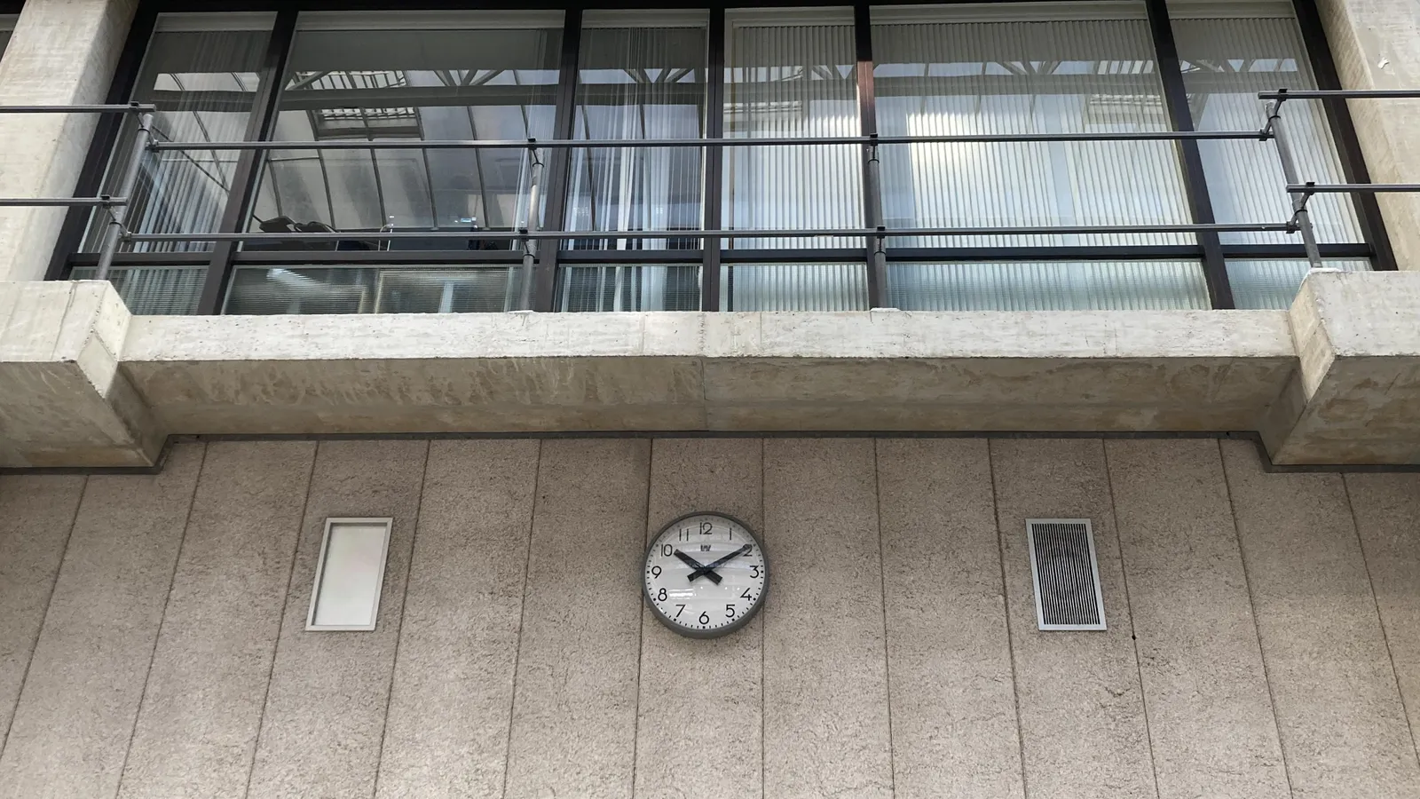A clock on a conctrete wall. It points at 9 minutes past 10.
