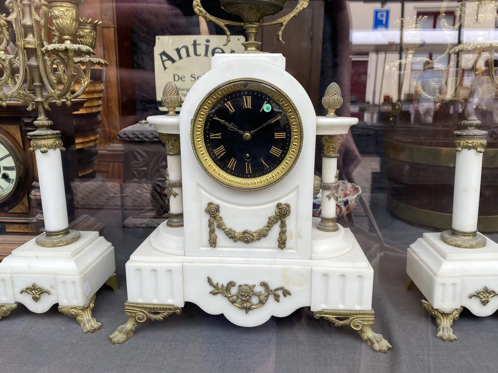 A white marble, and golden mantel clock, with two accompanying candlesticks, also made from white marble, richly ornamented. The clock points at 9 minutes past 10.