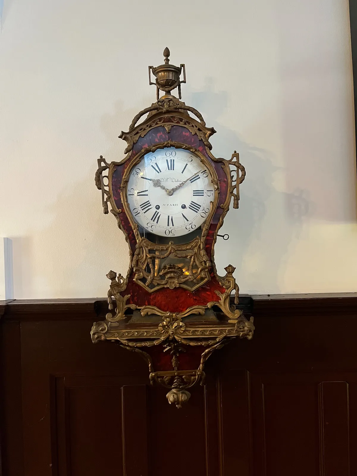 An old wall clock, ornamented with metal, and some shiny red parts. It points at 9 past 10.