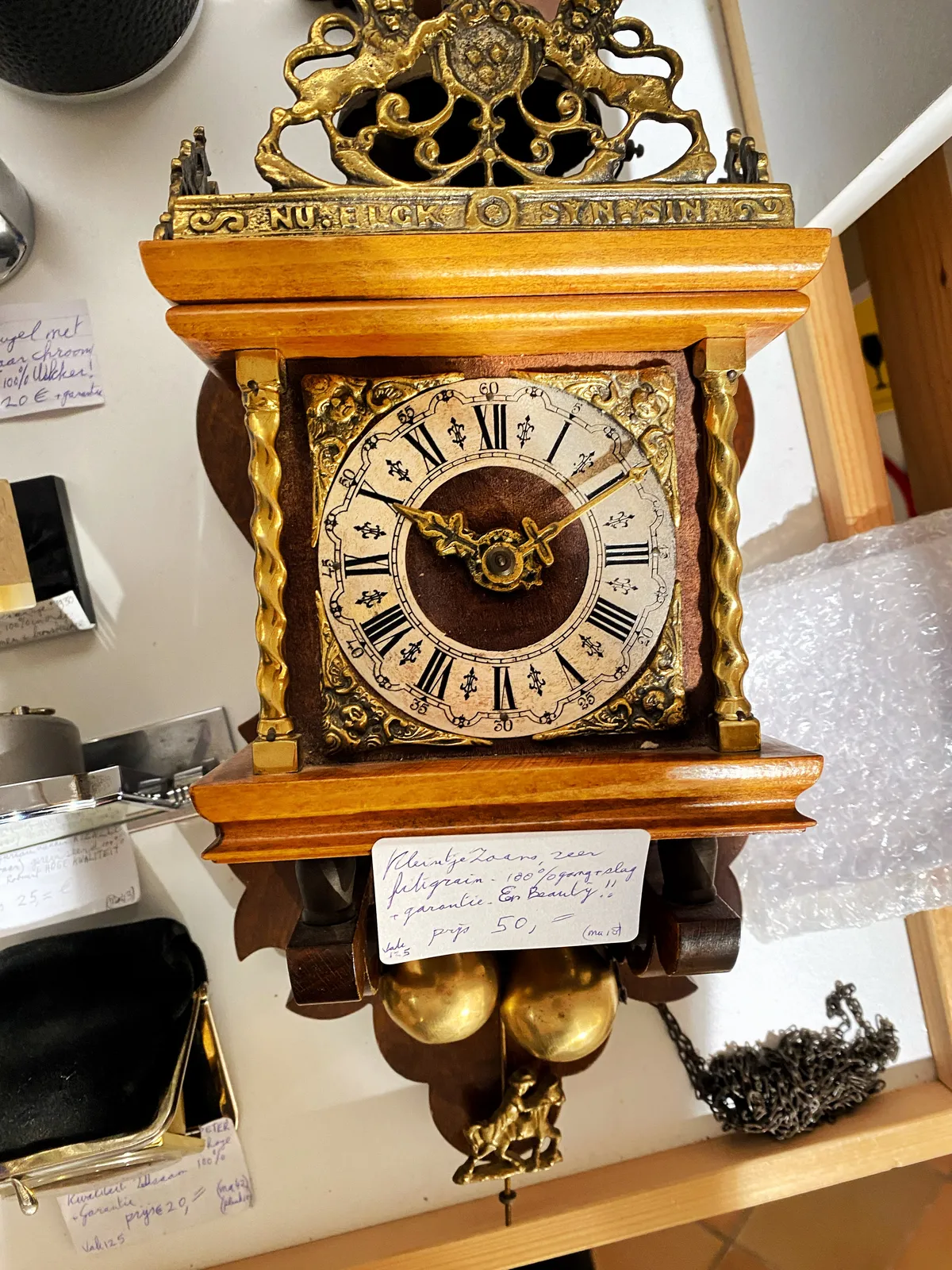 An old wooden clock, with a handwritten sign attached to it with a promotional description and the price: 50 euros. The clock points at 10 past 10.