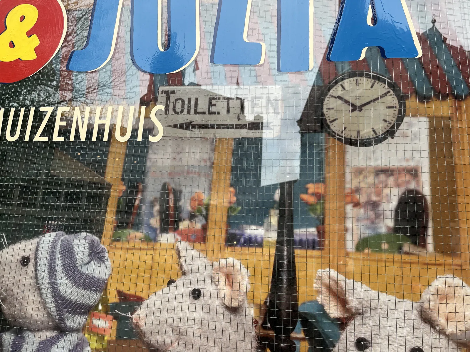 Behind steel enforced glass there’s a scene of plush mice. On the window the word Julia and the word Muizenhuis are painted. Muizenhuis means Mice House in Dutch. In the background of the scene there’s a station clock which points at 10 past 10.