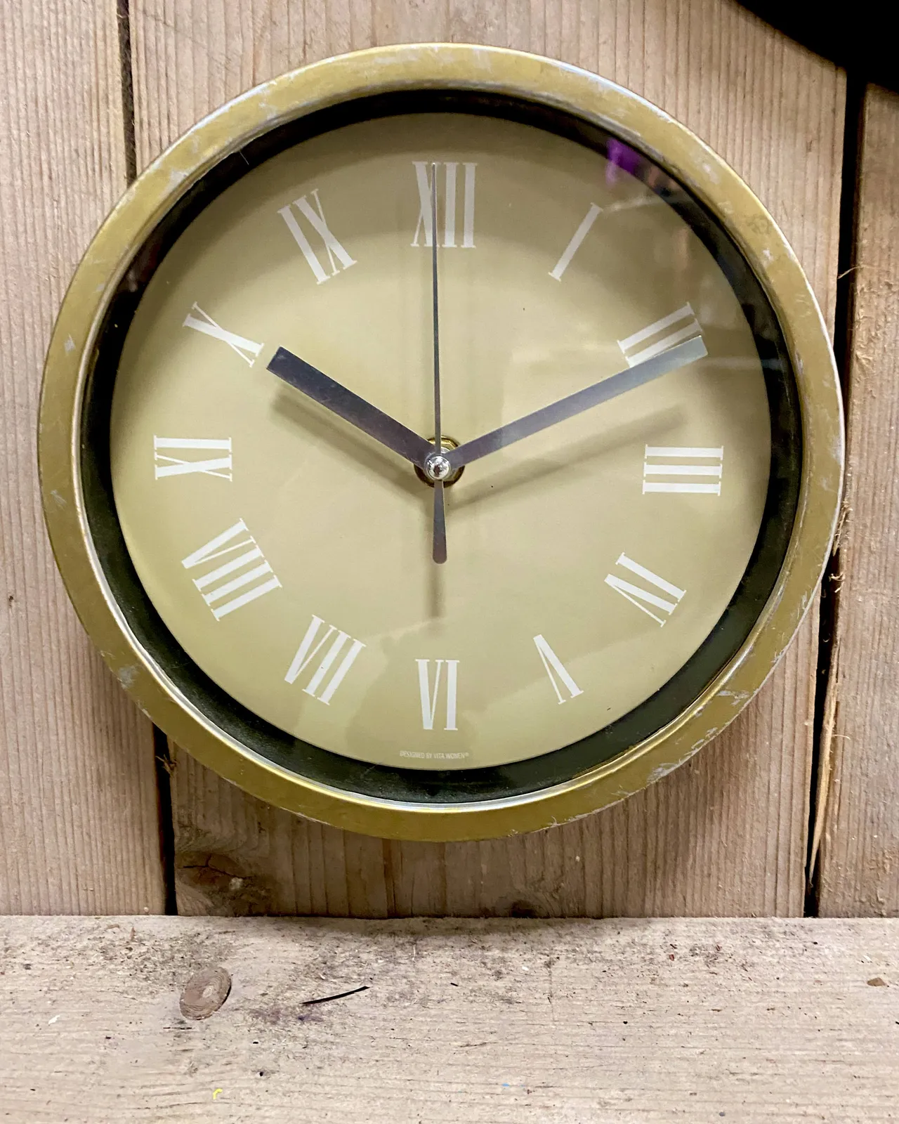 A simple dull light green clock on a wooden panel. It points at 11 past 10.