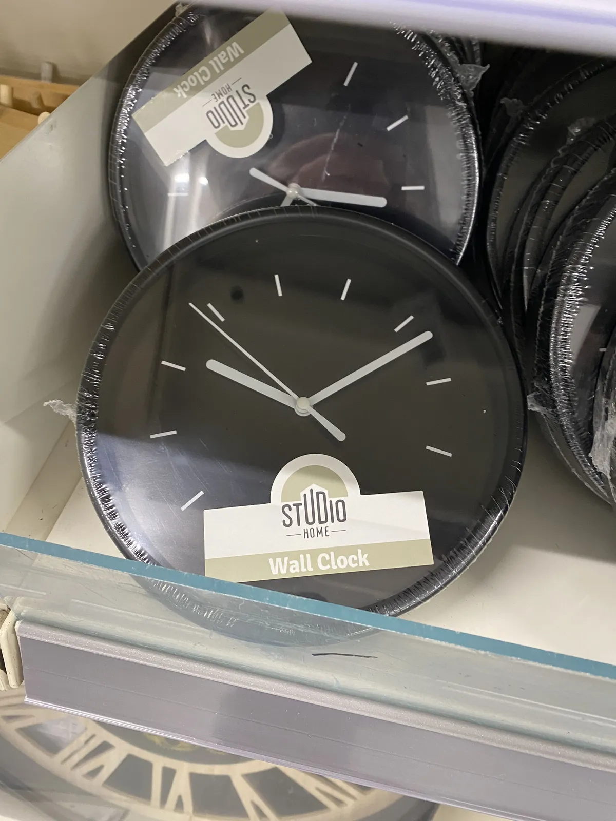 A cheap plastic wall clock, still wrapped in plastic, points at 12 past 10.
