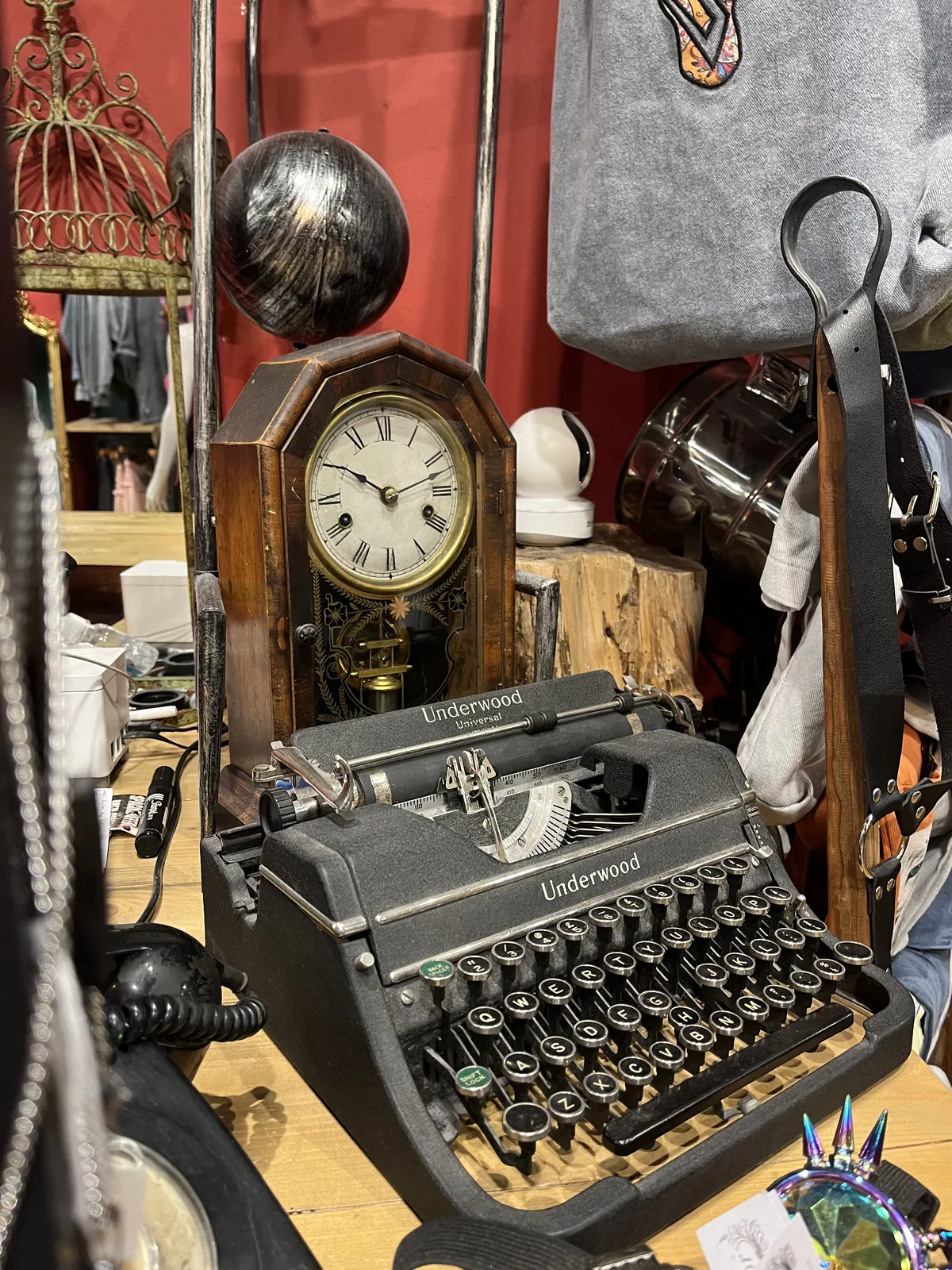 An old mechanical underwood typewriter, a rotary phone, and small, old, wooden standing clock. It is 12 minutes past ten on this clock.