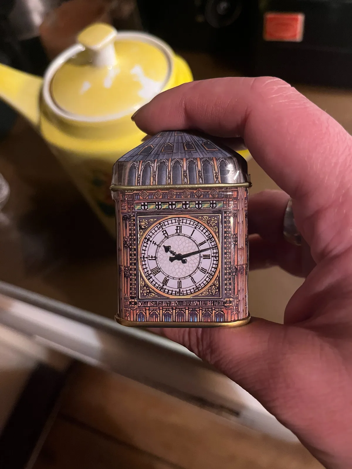 Someone is holding a small tin can in the shape of the top of the Big Ben tower, the part with the clock on it. The clock point at 12 past 10.