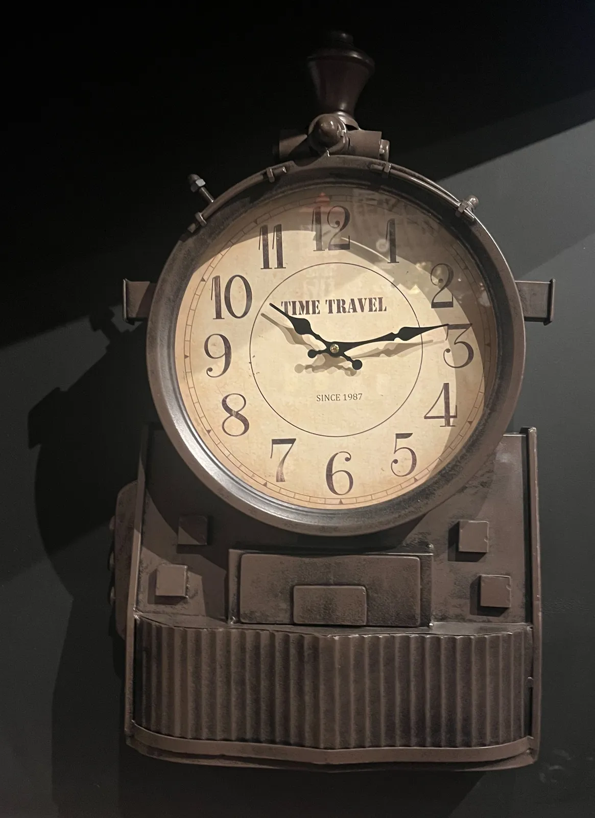 A clock in a cyber punk frame with the words Time Travel since 1987 on its face. It points at 13 minutes past 10.