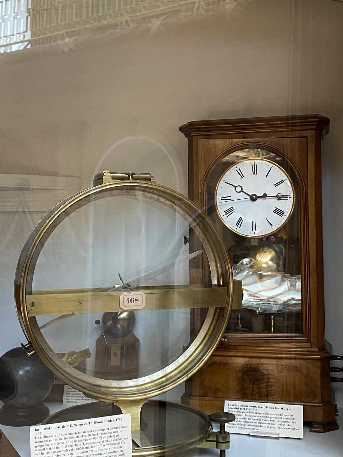 A clock on display in a museum. It looks like an old wooden mechanical clock, but the sign says it is an old electrical clock built in 1847! It points at 14 past 10.