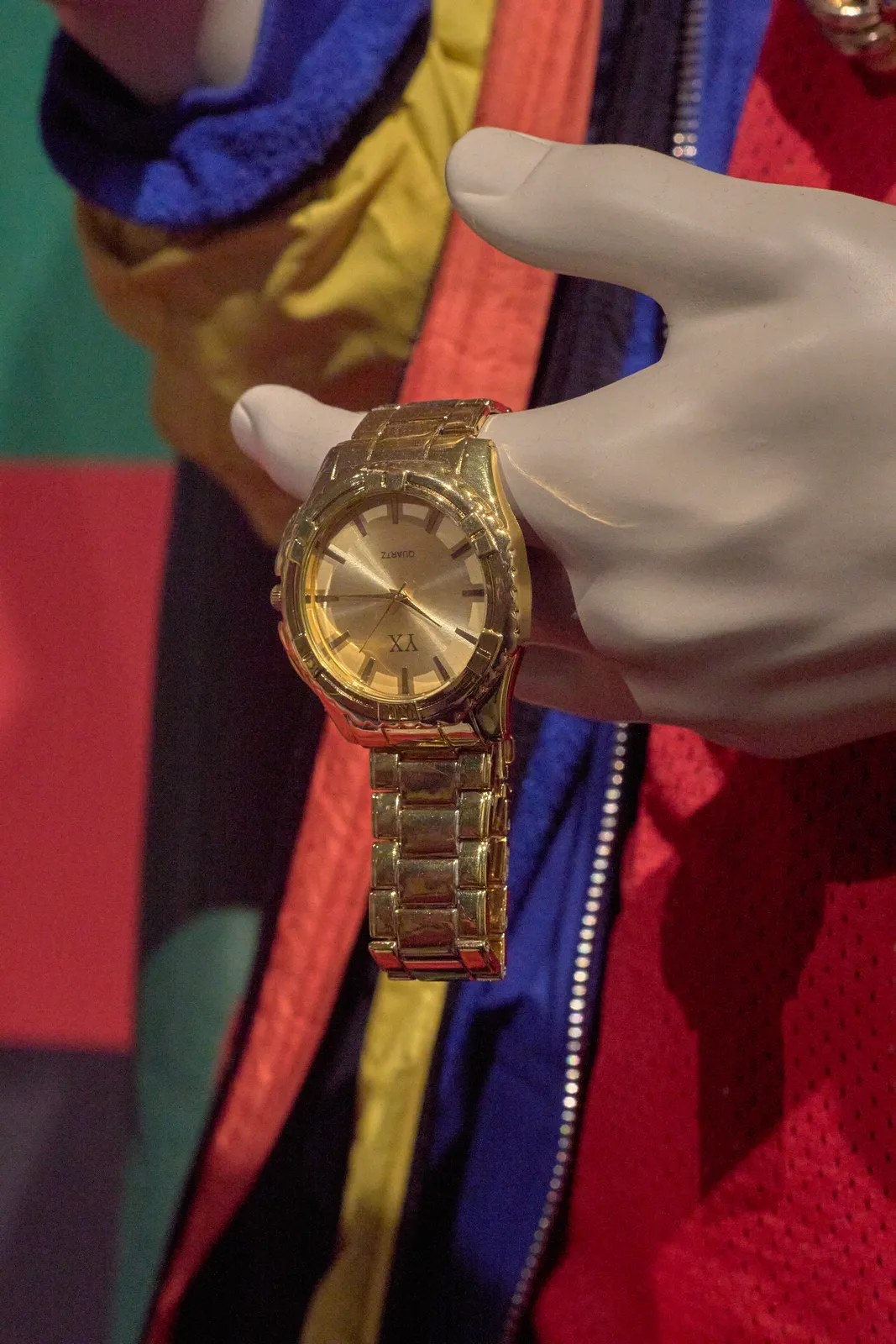 It seems like someone, dressed in colourful clothes, is holding gold watch in their hands, but on further inspection this someone turns out to be a tailor's dummy. The watch points at a quarter past ten.
