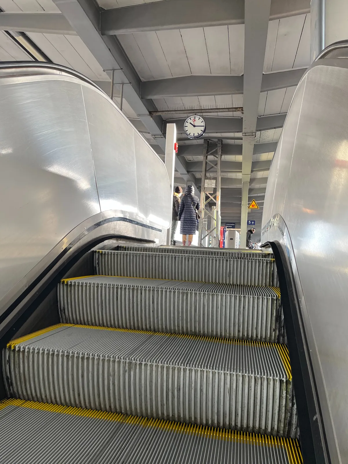Rolling up the escalator, onto a train platform. The clock on the platform points at a quarter past 10.