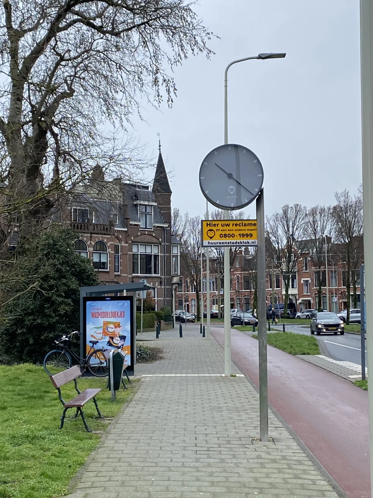 A clock attached to a street light in what seems to be a chic part of town in a Dutch city. The clock points at 22 past 10.