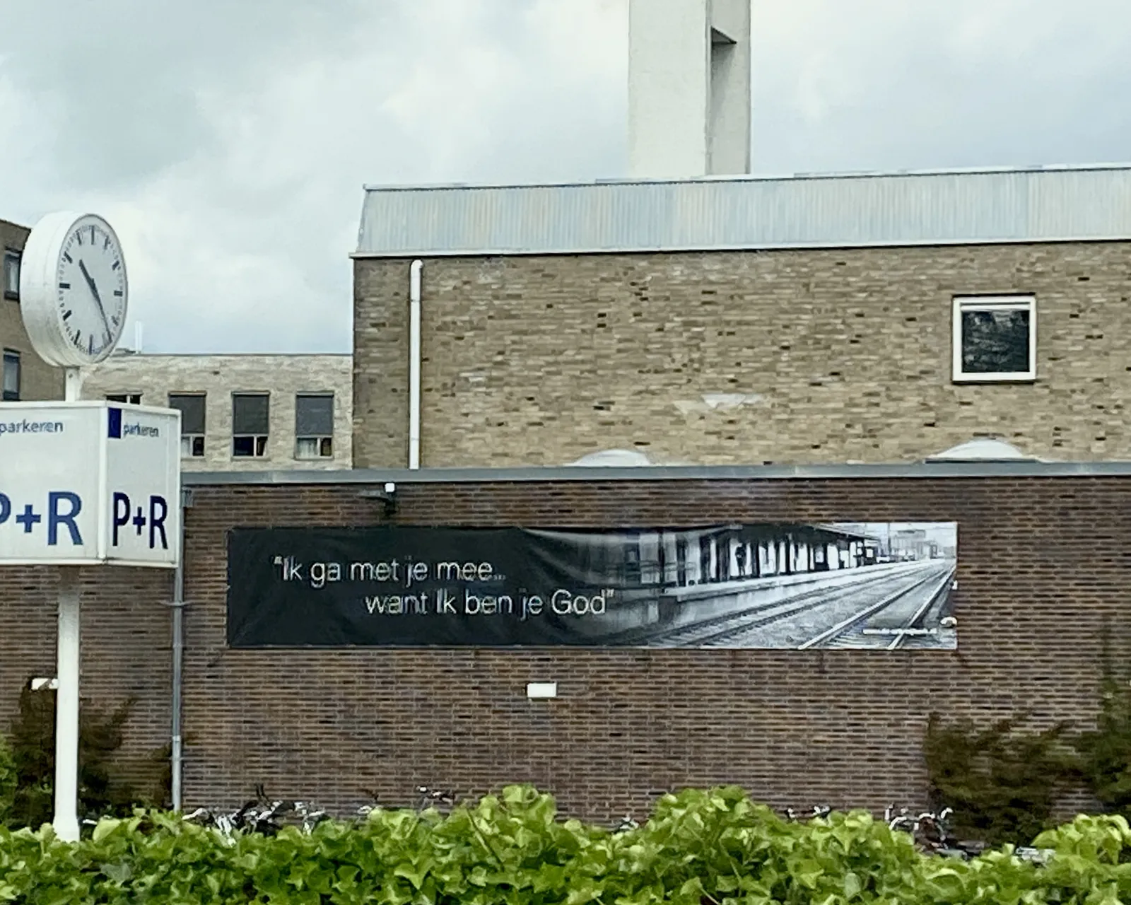 A rather confusing sign on a modern brick church next to a train station. It says (translated from Dutch) I will come with you because I am god. There’s also a clock on this picture. It points at approximately 23 minutes past 10.