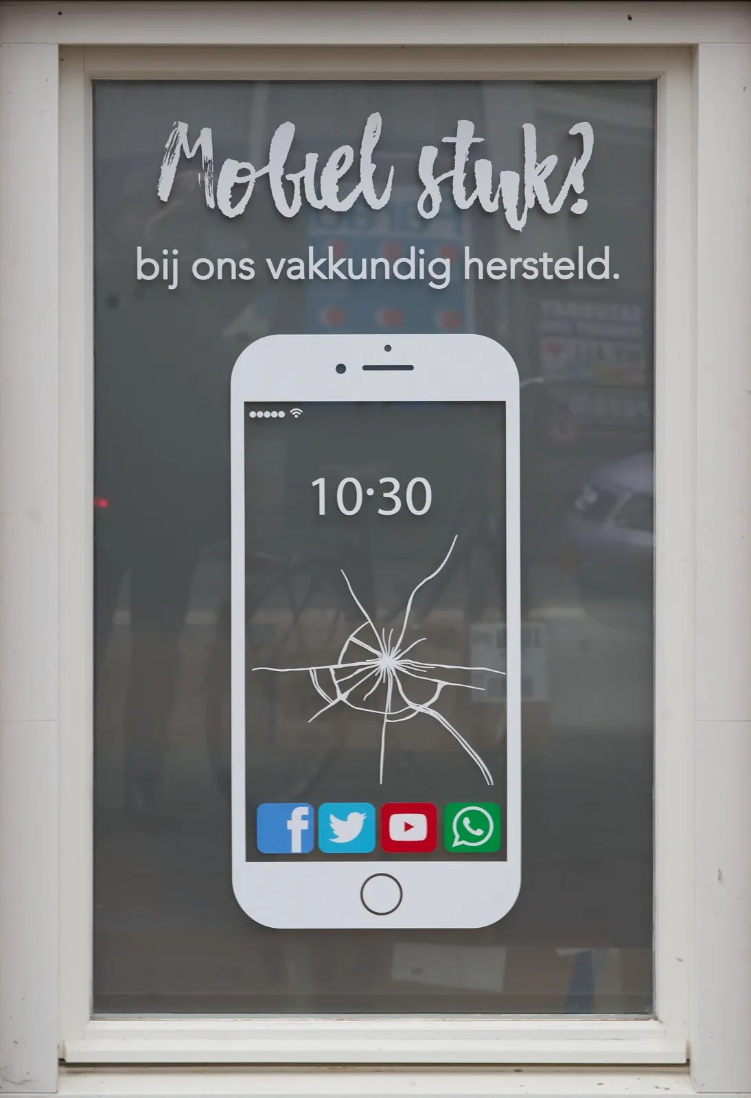 On a window of a phone repair shop there’s a large sticker of an abstracted phone with the time on it: 10:30 