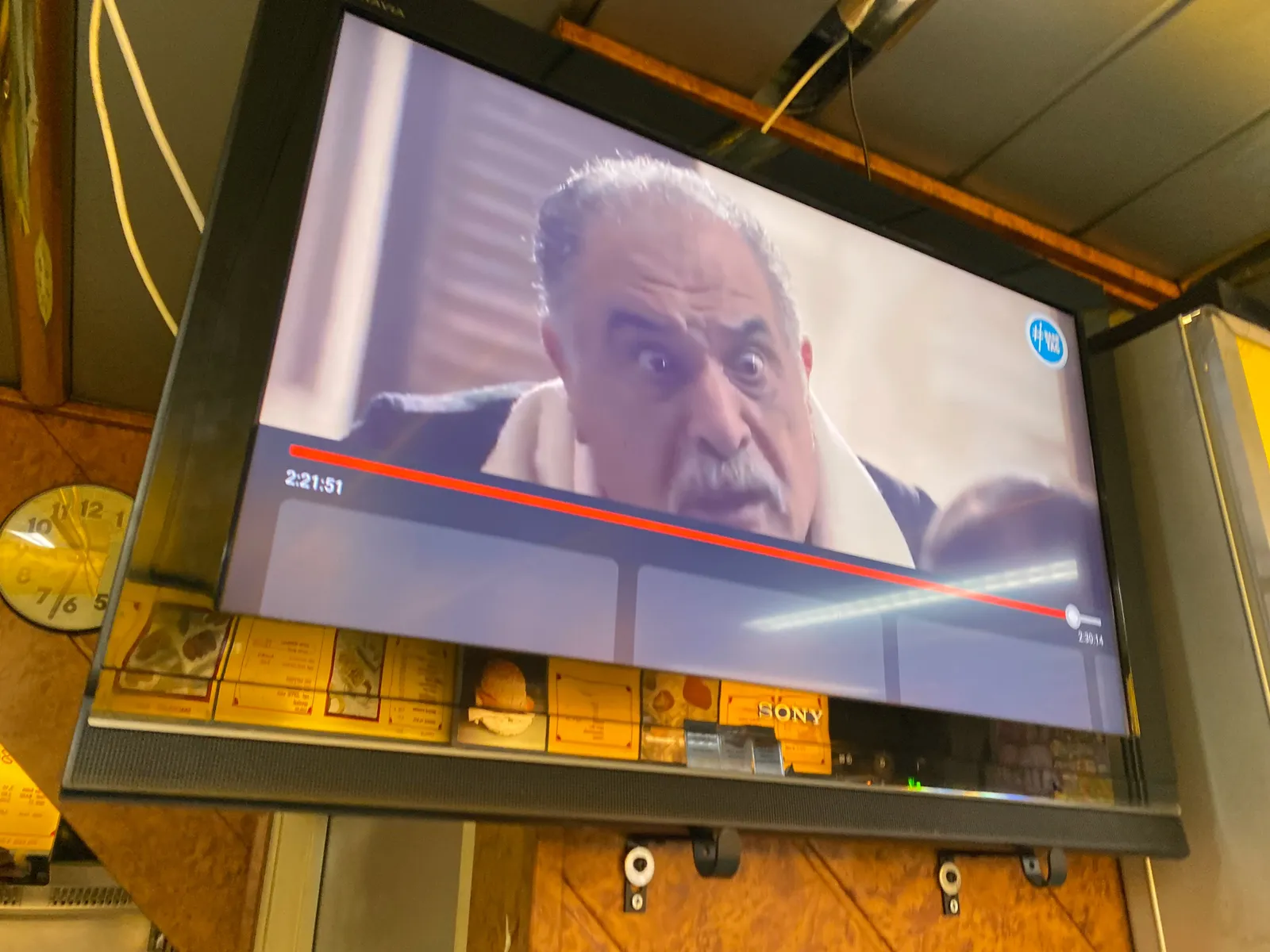 A large screen shows a man with a surprised expression. Behind the screen is a clock which points at 32 minutes past 10.