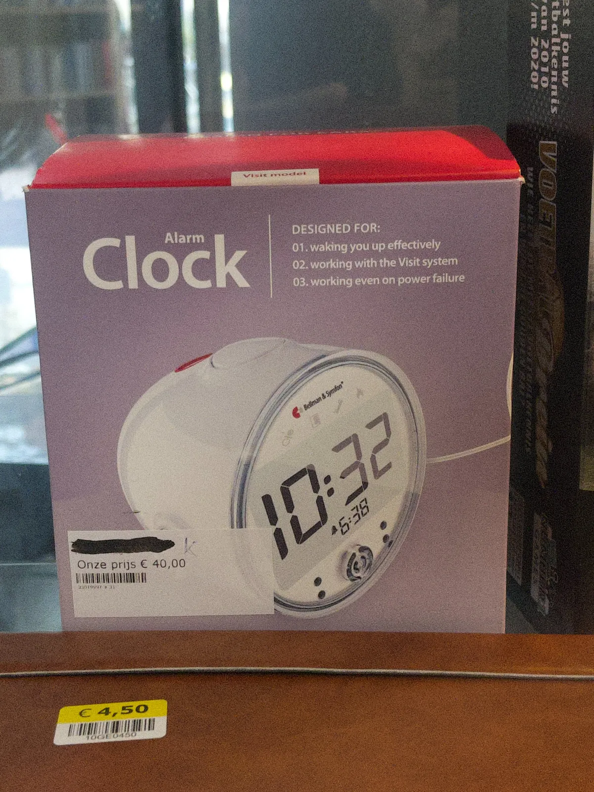 A picture of a digital alarm clock on a box. It says it is 10:32.