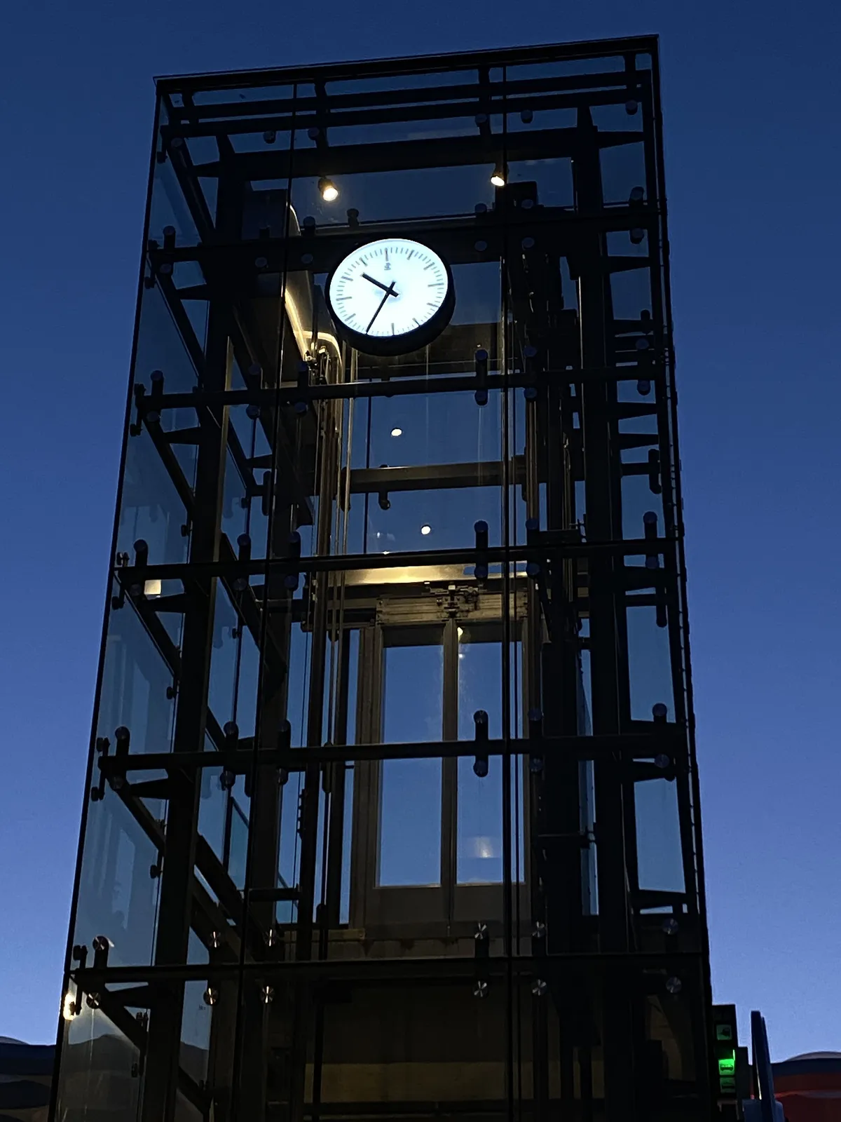 A clock on a glass elevator tower points at 25 minutes to 11.
