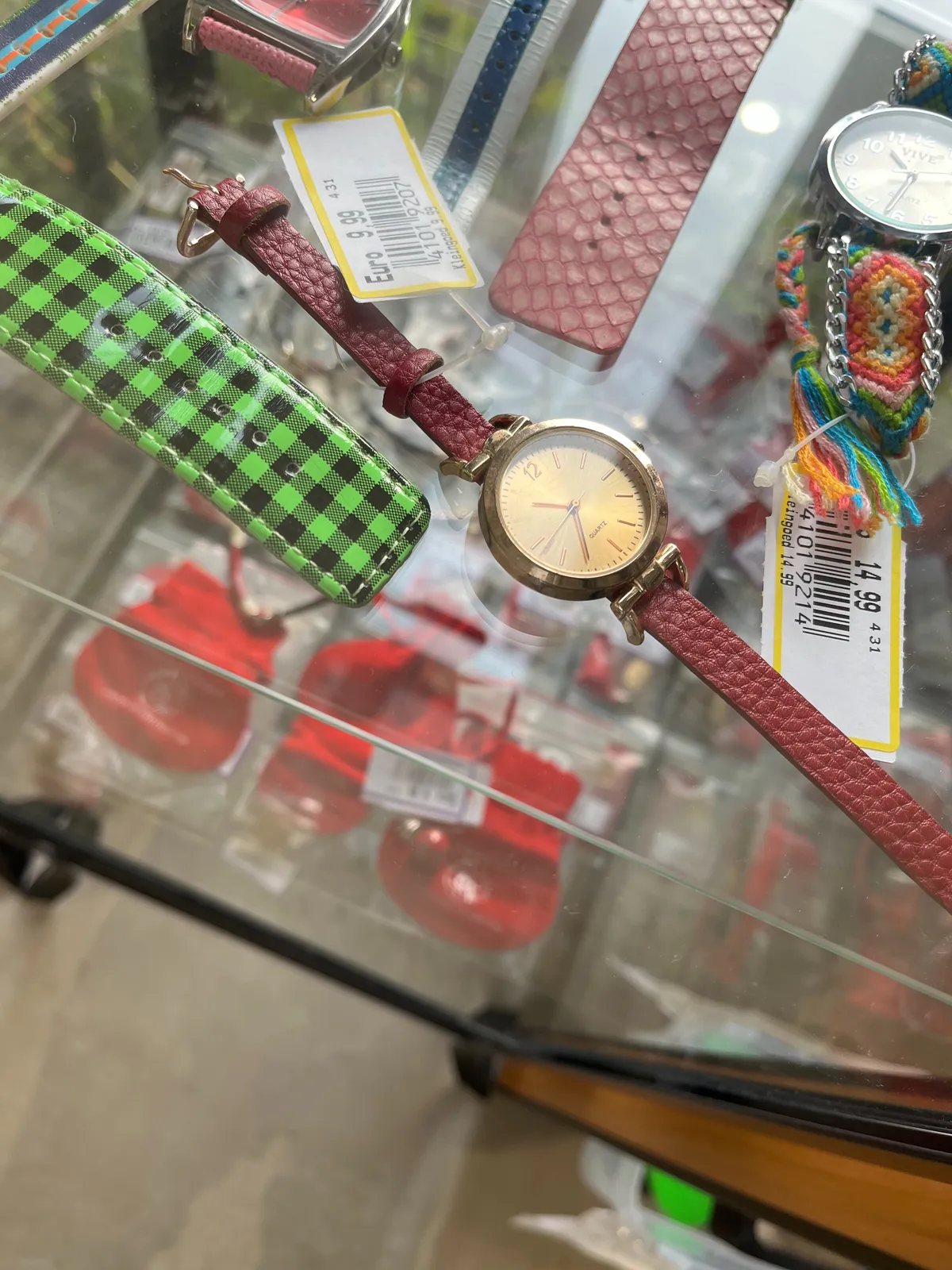 A gold looking wrist watch with a red strap for sale for 9 euros and 99 cents. It points at 36 minutes past 10.
