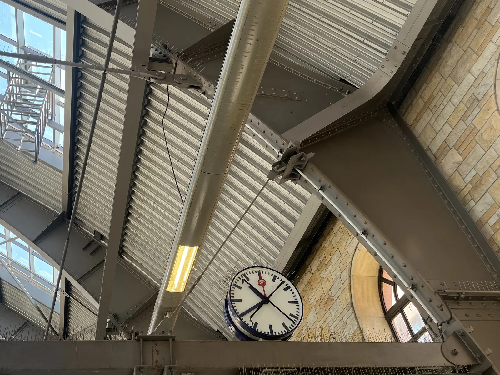 A station clock with an X taped onto its face. Behind it part of the dome of the station. It points at 20 minutes to 11.