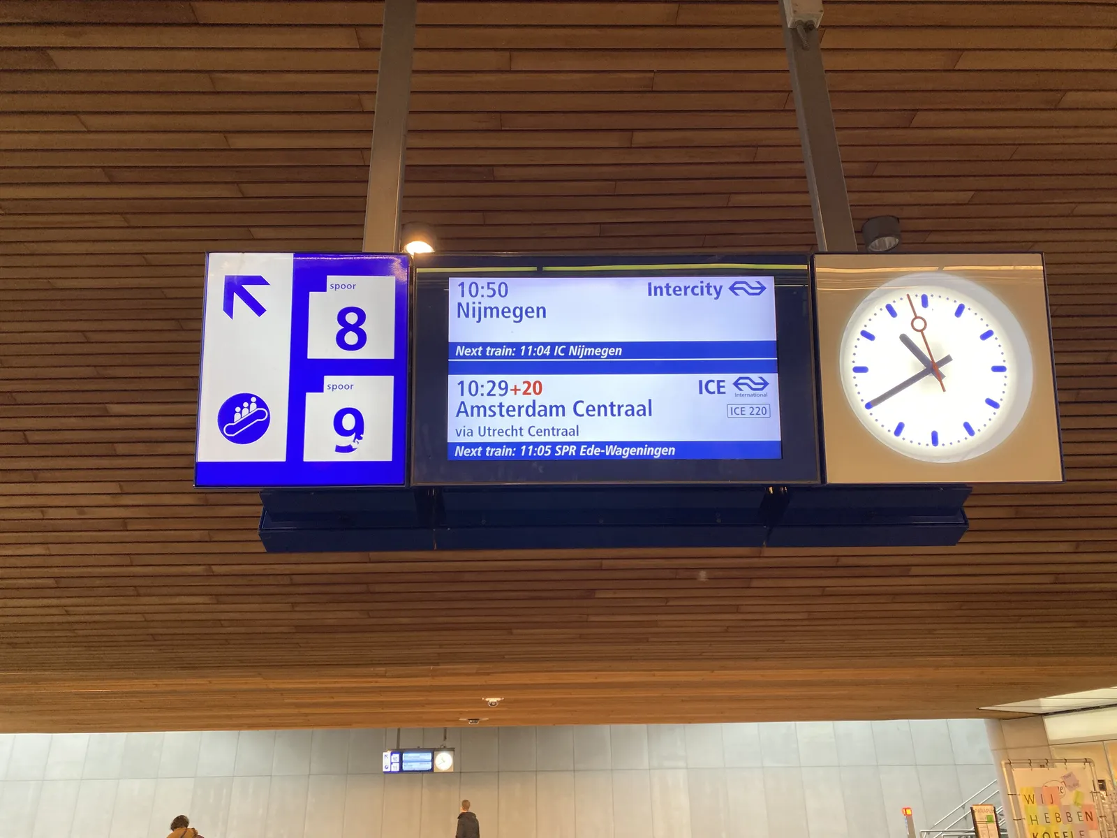 A digital sign in a Dutch train station. Trains to Nijmegen and to Amsterdam will be leaving shortly from platform number 8 and 9. The clock attached to this sign pionts at 20 minutes to 11.