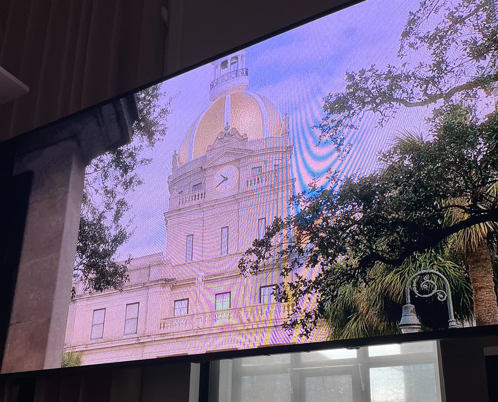 A building is projected on an enormous LED display. This screen is absolutely gigantic. On the building there’s a clock which points at 20 minutes to 11.