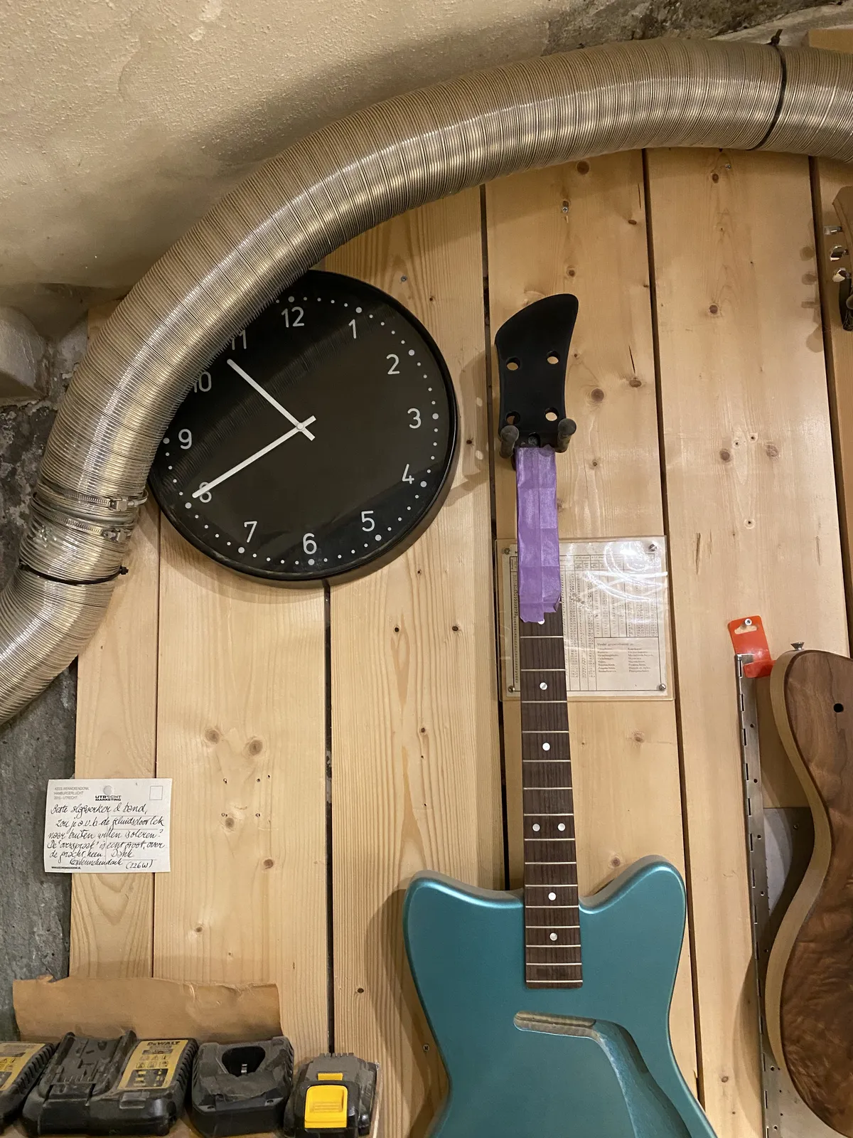 A clock on a wall in a guitar workshop, next to a funky blue guitar. It points at 20 to eleven.