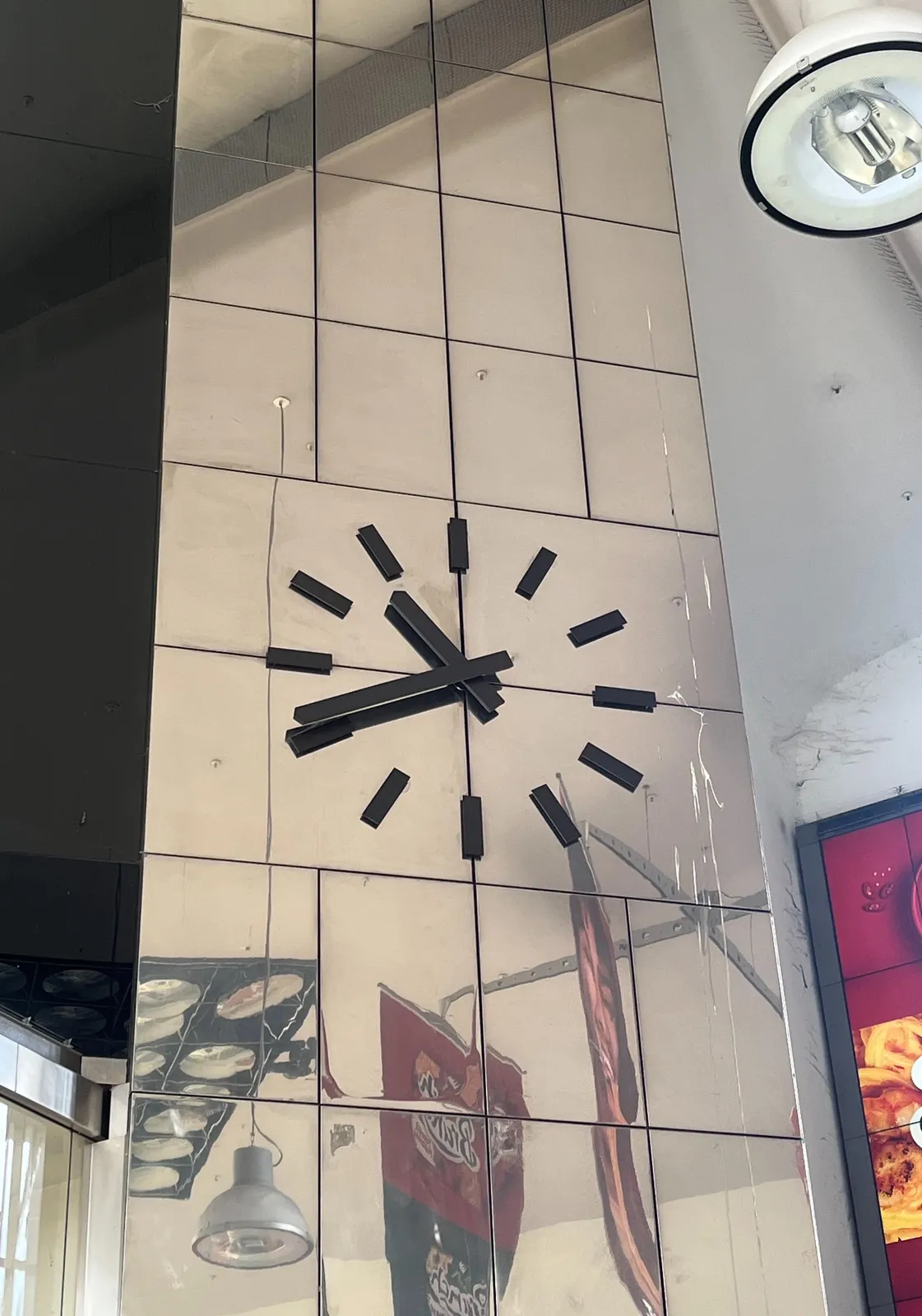 A large clock on a very large, multiple stories high mirror. The mirror is not very well made, the things it reflects are morphed into unidentifyable blobs. The clock on this mirror points at 19 minutes to eleven.